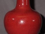 a red vase sitting on a table with a lamp on it