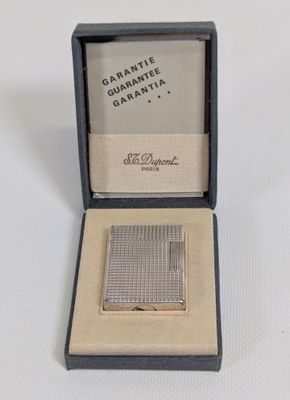 un petit étui à cigarettes en argent, posé dans une boîte sur une surface blanche