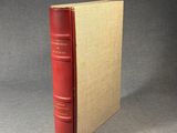 an old red book sitting on top of a table next to a gray wall