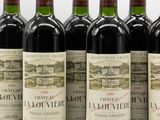 six bottles of red wine lined up in a row on a white surface