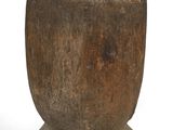 une vieille tasse en bois posée sur un socle, sur une surface blanche