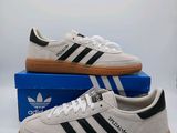 une paire de baskets Adidas blanches et noires posées sur une boîte bleue