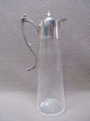 un pichet en verre transparent muni d'une anse en argent, posé sur une table