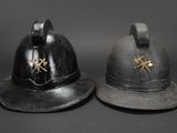 pair of antique fireman ' s helmets on display against a black background