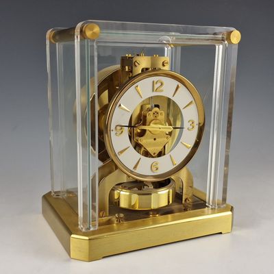 une horloge dorée dans un écrin transparent posé sur une surface blanche
