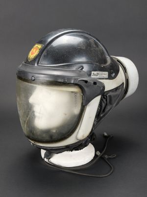 un vieux casque noir et blanc posé sur un support, sur fond noir