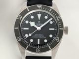 La montre est dotée d'un cadran noir et d'un bracelet en cuir noir.