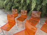 six orange plastic chairs sitting in front of a bush of trees