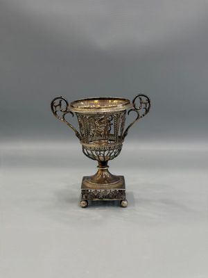 an antique silver cup on a stand on a white surface