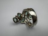 a close up of a silver ring with green stones on a white surface