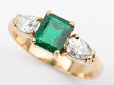 an emerald and diamond three stone ring on a white background