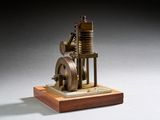 une petite maquette de machine à vapeur posée sur un socle en bois