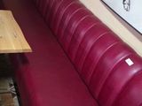 a red leather bench in a restaurant with a painting on the wall behind it