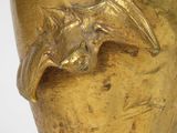 a gold vase with a bird on it on a white surface