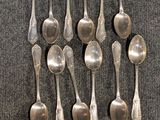 six cuillères en argent sont disposées en rang sur une surface grise