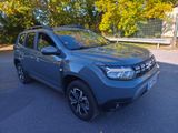 a grey dacia parked in a parking lot with trees in the background