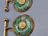 two gold and green cufflinks with a coin on them