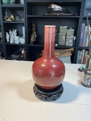 un vase rouge posé sur une table devant une bibliothèque