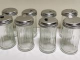 six salières et poivrières en verre alignées sur une table