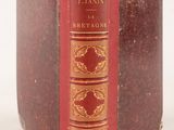 an old book with a red cover sitting on top of a white surface