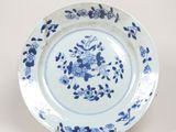 assiette bleue et blanche ornée de fleurs et de feuilles, posée sur un socle