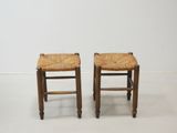 pair of wooden stools with woven seats against a white wall
