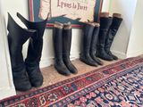 Plusieurs paires de bottes sont alignées contre un mur, près d'un tapis