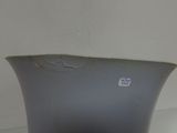 a gray vase sitting on a table with a white wall behind it