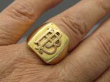 a man ' s hand holding a gold ring with a symbol on it