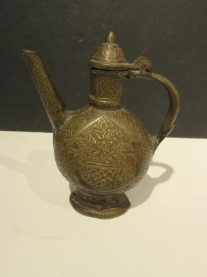 an antique brass teapot on a white table with a black background