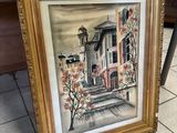 painting of a house in a gold frame sitting on a tile floor