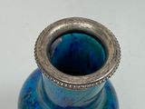 a blue vase with a silver rim sitting on a table
