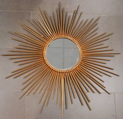 un miroir doré à rayons, posé à même le sol dans une pièce
