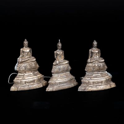 three silver figurines of buddhas sitting on top of a table