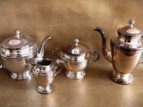 three silver teapots and two silver cups on a table