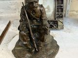 une statue en bronze représentant un soldat assis sur un rocher, un fusil à la main