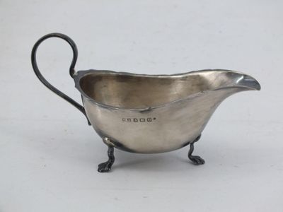 an antique silver plated sauce boat with a handle on a stand