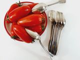 tomatoes in a bowl with forks and spoons on a white surface