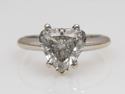 un gros plan d'une bague en diamant en forme de cœur posée sur une surface blanche