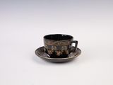a black and gold cup and saucer sitting on a white surface