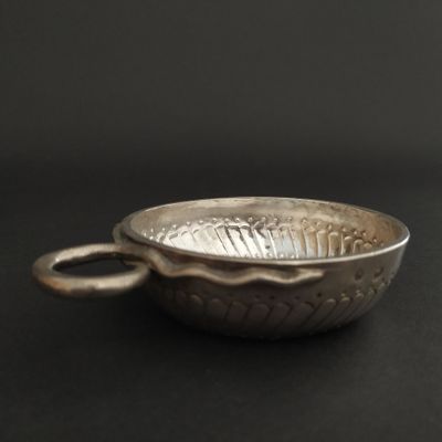 a silver bowl with a handle on a black surface
