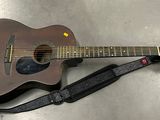 une guitare posée par terre, avec une sangle autour
