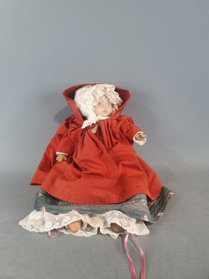 une vieille poupée vêtue d'une robe rouge et d'un bonnet, assise sur une table