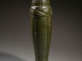 a green vase sitting on top of a table next to a wall