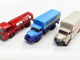 trois camions miniatures posés les uns à côté des autres sur une surface blanche