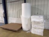 une pile de rouleaux de plastique blancs posée par terre à côté d'un carton
