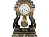 une horloge noire et dorée posée sur un socle, sur fond blanc