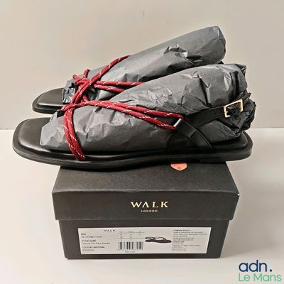 une paire de sandales noires avec un lacet rouge noué sur le dessus, posée sur une boîte