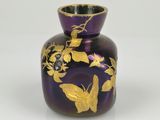 purple vase with gold butterflies and flowers on it on a white surface