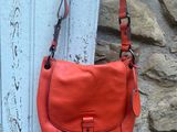 un sac à main orange accroché sur le côté d'une porte, près d'un mur en pierre